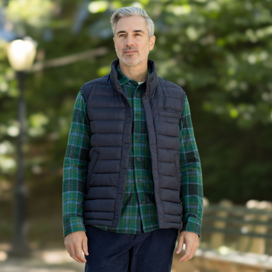 Man wearing an adaptive magnetic navy puffer vest over a green plaid shirt outdoors.