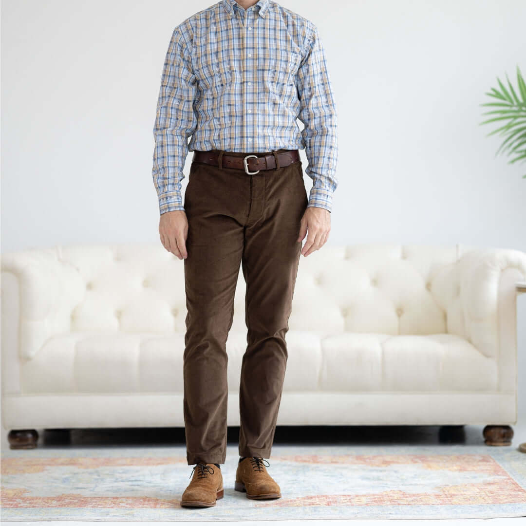 Man wearing adaptive brown fine whale corduroy pants with a magnetic fly and checkered shirt, standing in a stylish living room.