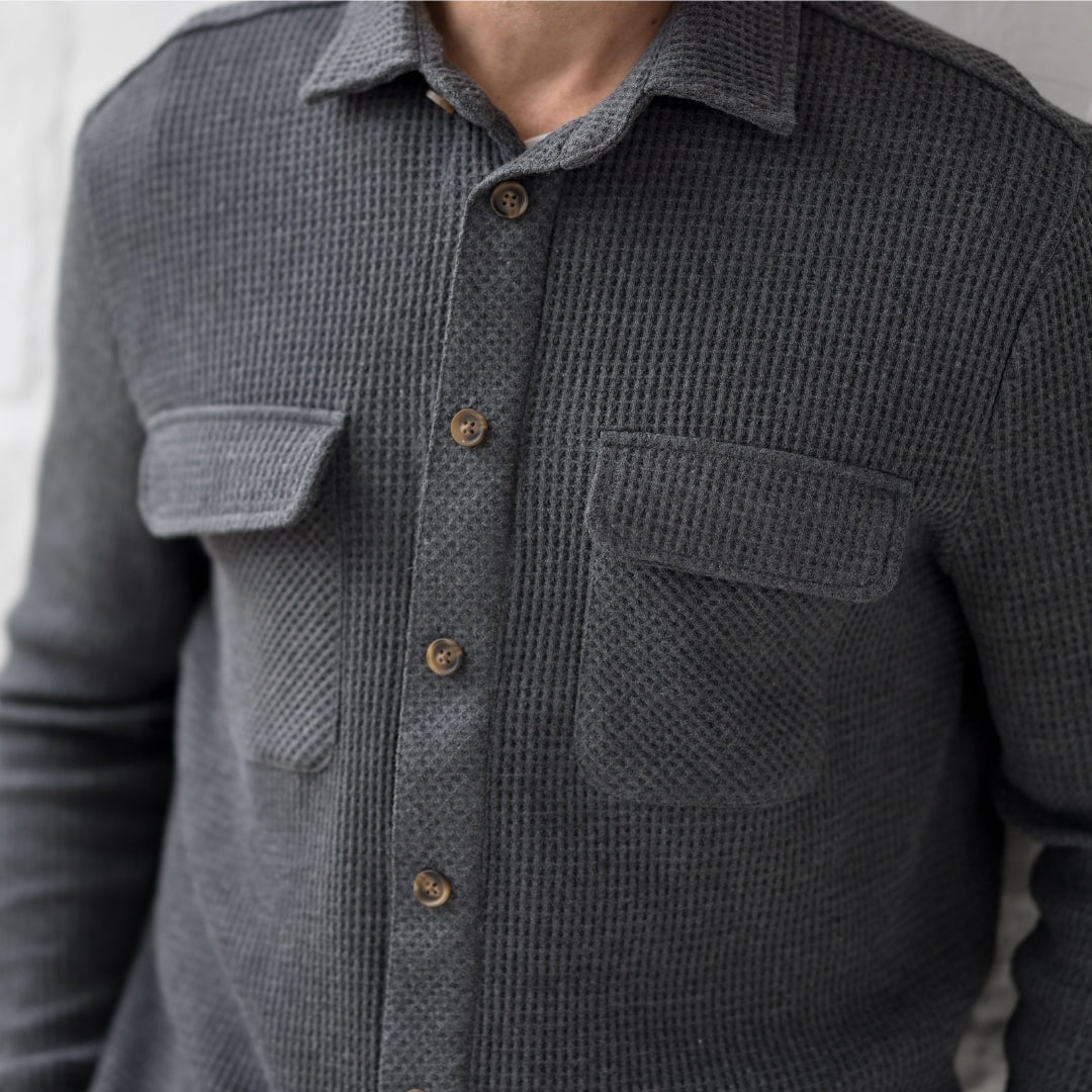 Close-up of a man wearing a stylish gray button-up shirt with pockets and a textured fabric.