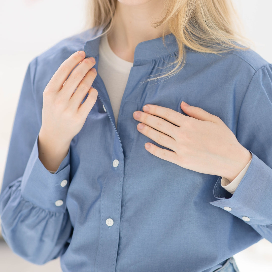 Close-up of a person in a blue button-up shirt adjusting the collar, highlighting casual style and comfort.