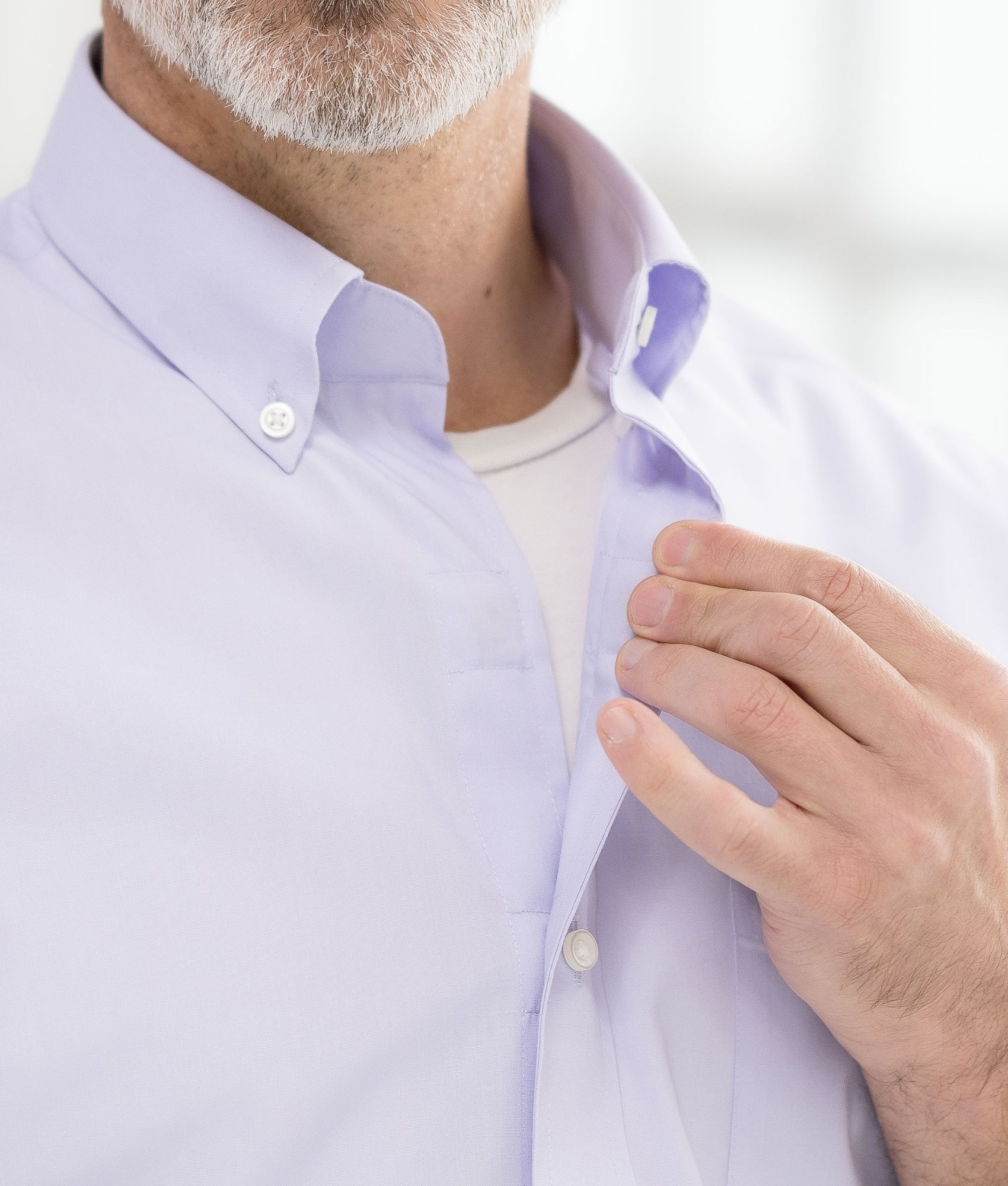 Close-up of a man adjusting the collar of a light purple dress shirt, showcasing style and fabric quality.