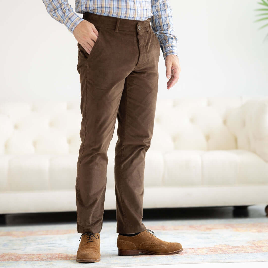 Man wearing brown adaptive corduroy pants, showcasing magnetic fly design, standing in a bright room.