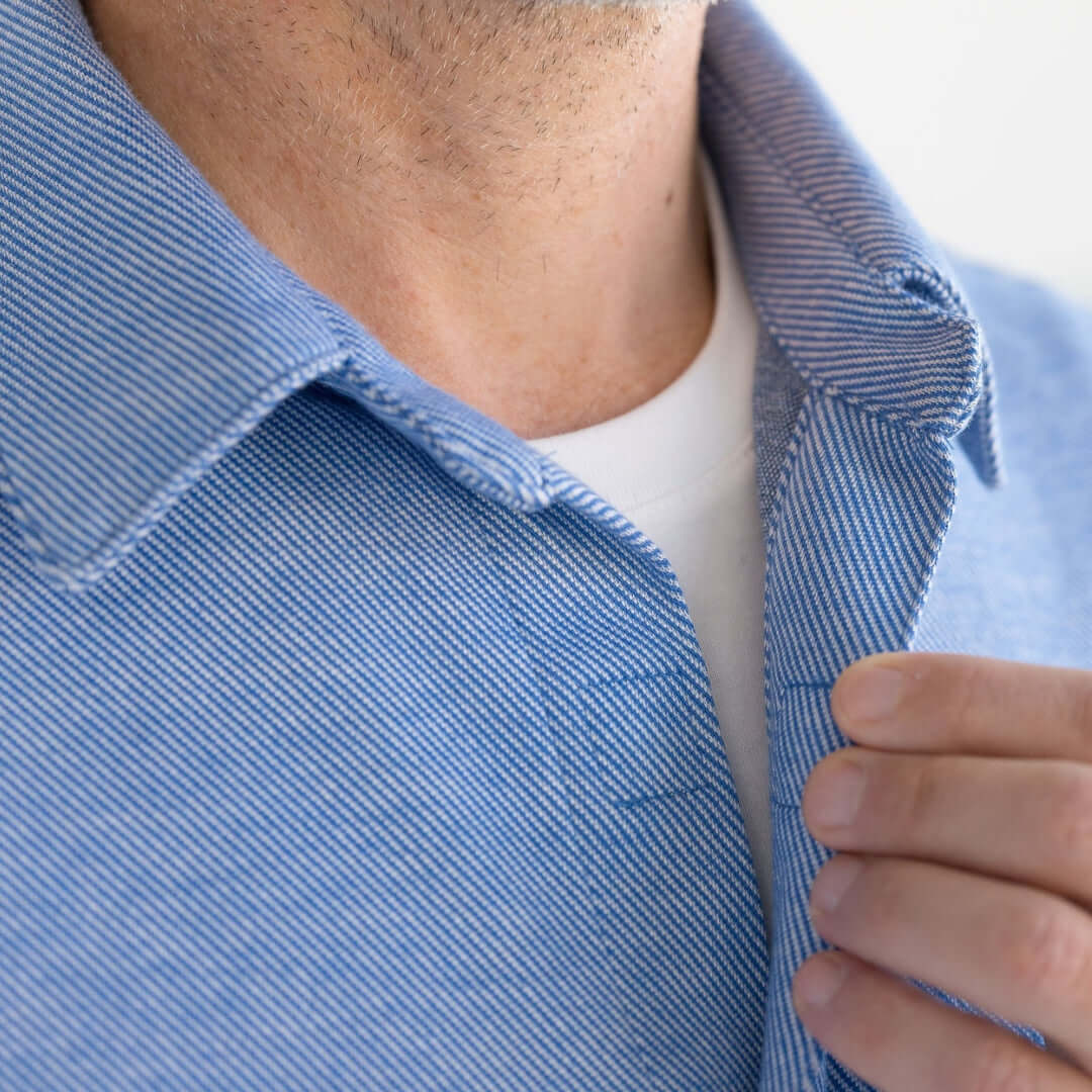 Close-up of a man adjusting the collar of a blue striped western shirt with magnetic buttons.