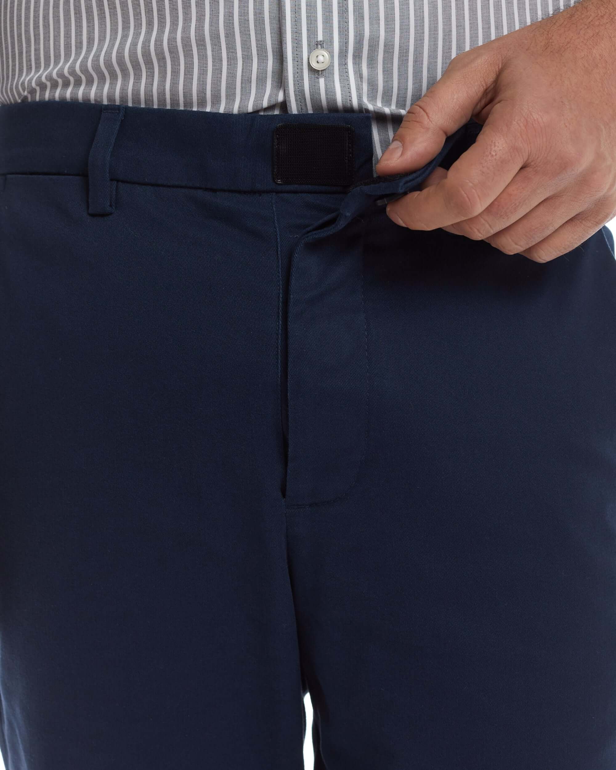 Close-up of a person fastening the magnetic closure of navy chino twill pants designed for adaptive wear.
