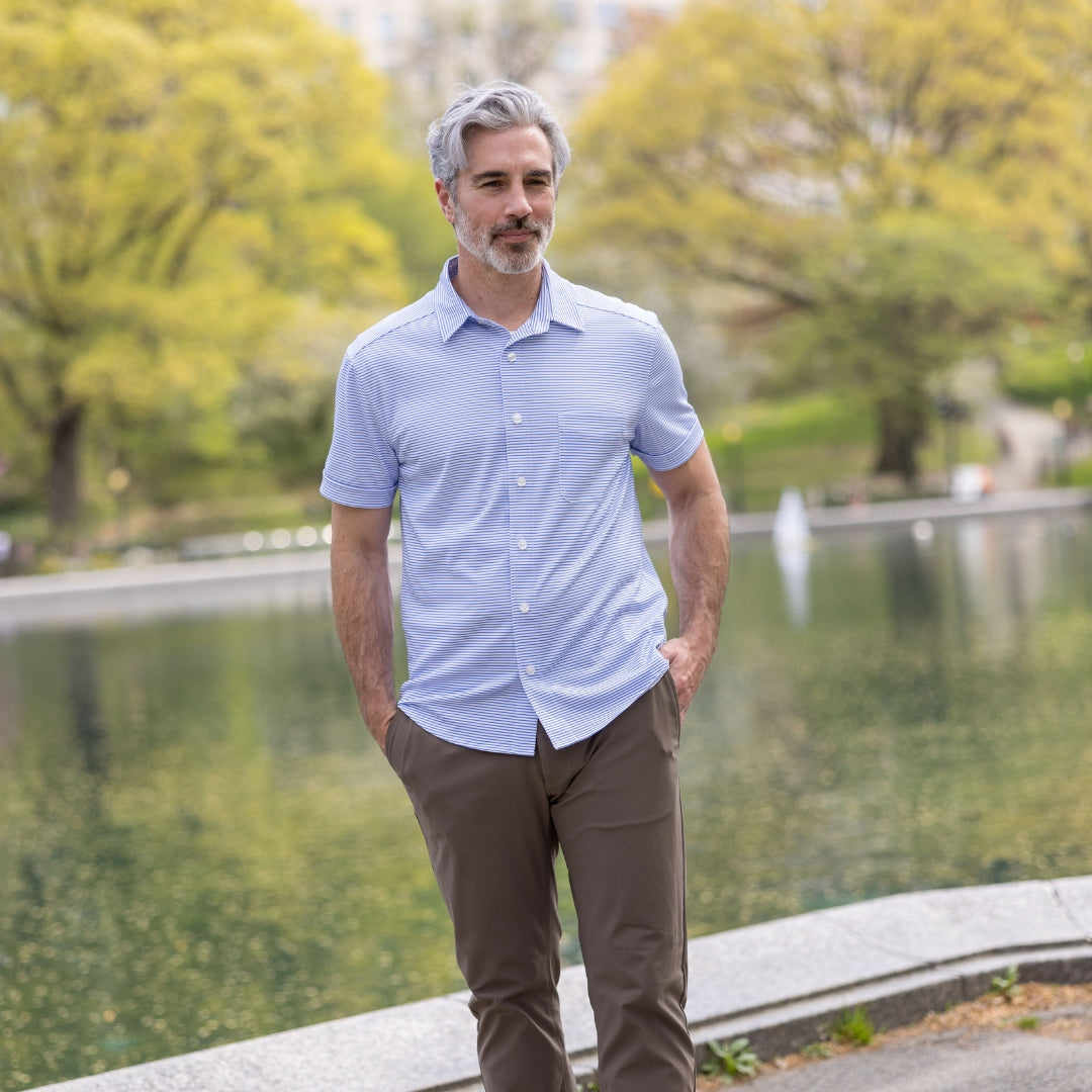 Adaptive Cooling Magnetic Front Short Sleeve Shirt in Blue Stripe worn by a man outdoors beside a tranquil water body.