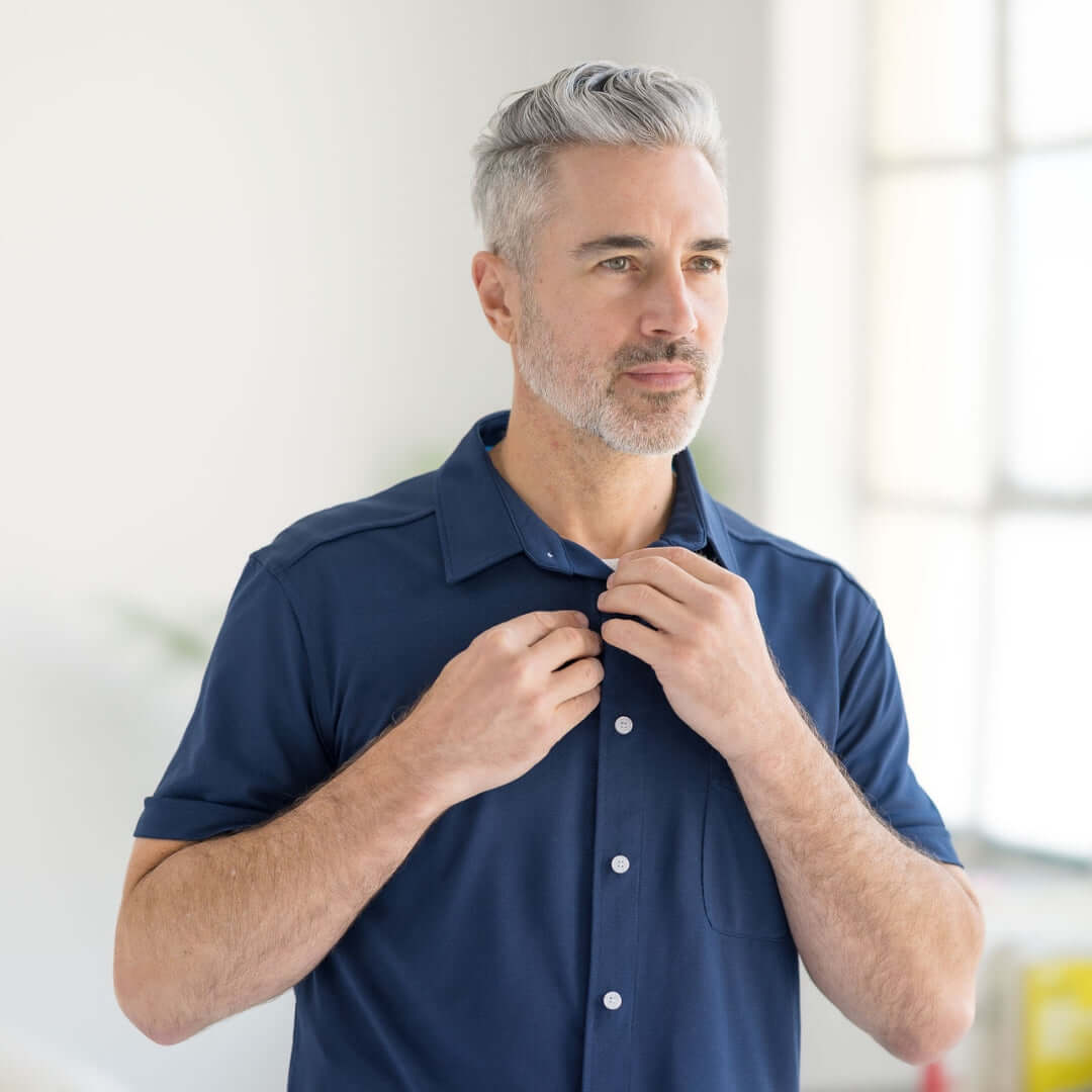 Man adjusting buttons on adaptive cooling magnetic shirt in navy, designed for comfort and limited mobility.