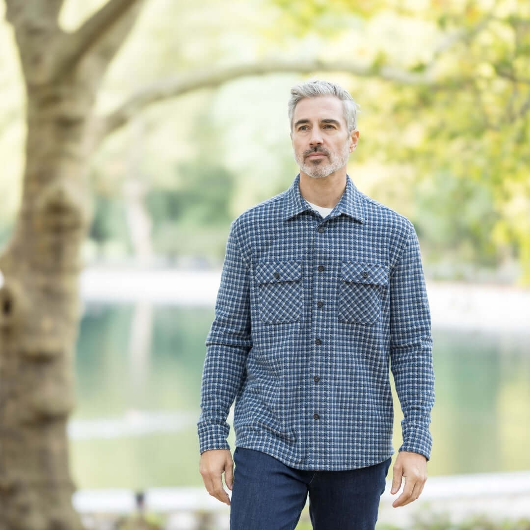 Man in a navy check flannel shirt standing outdoors near water, showcasing stylish layering piece for fall.