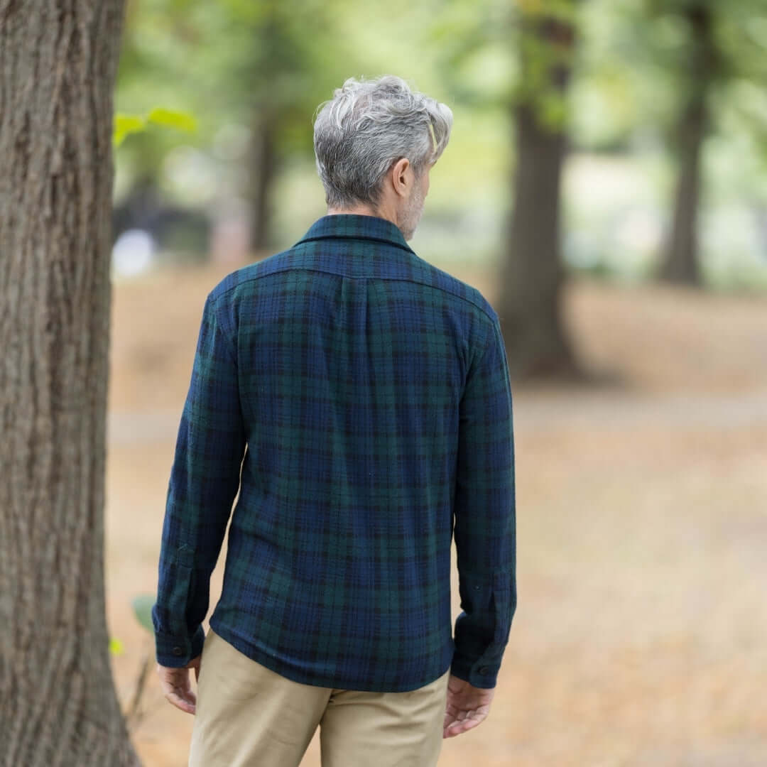 Man wearing an adaptive navy and green check flannel shirt, viewed from the back in a natural setting.