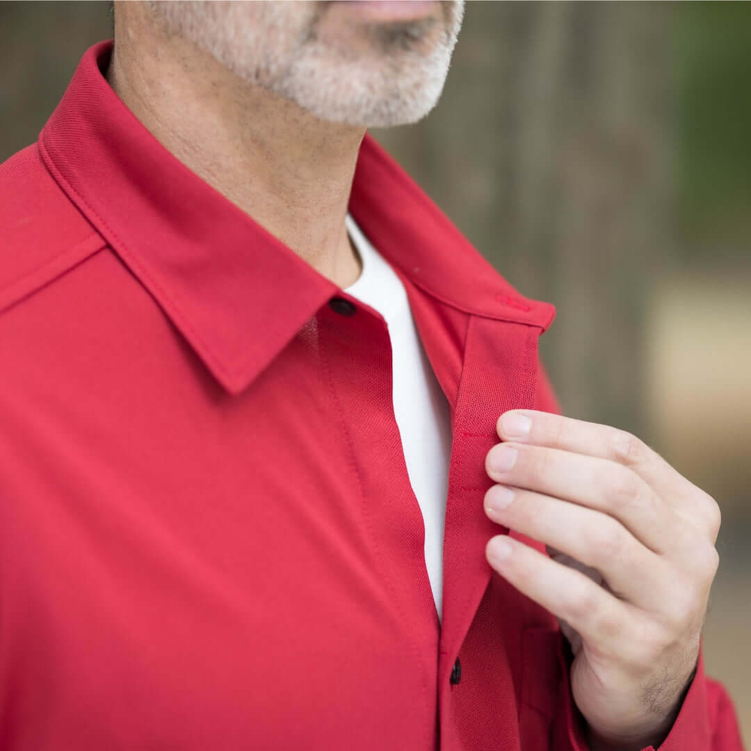 Close-up of a man in a red long sleeve polo shirt using magnetic buttons for easy closure.