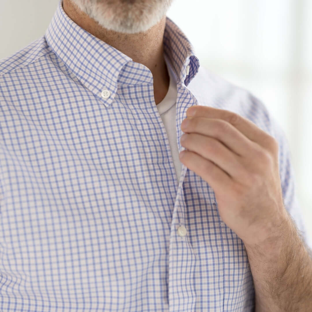 Close-up of a man adjusting a button-down collar shirt with a checked pattern and short sleeves.
