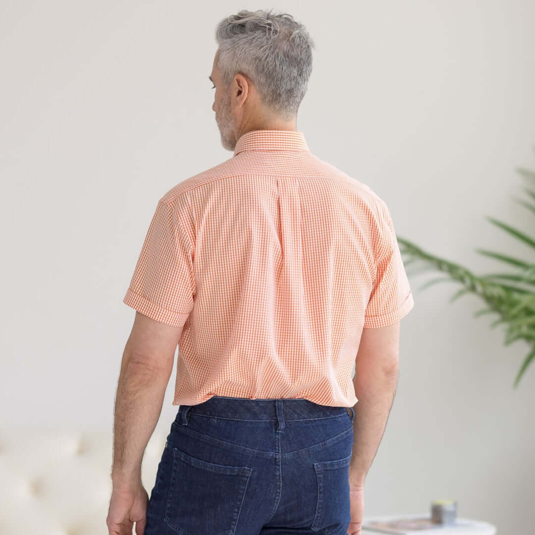 Back view of a man wearing a short sleeve orange and white gingham cotton shirt, ideal for adaptive fashion.