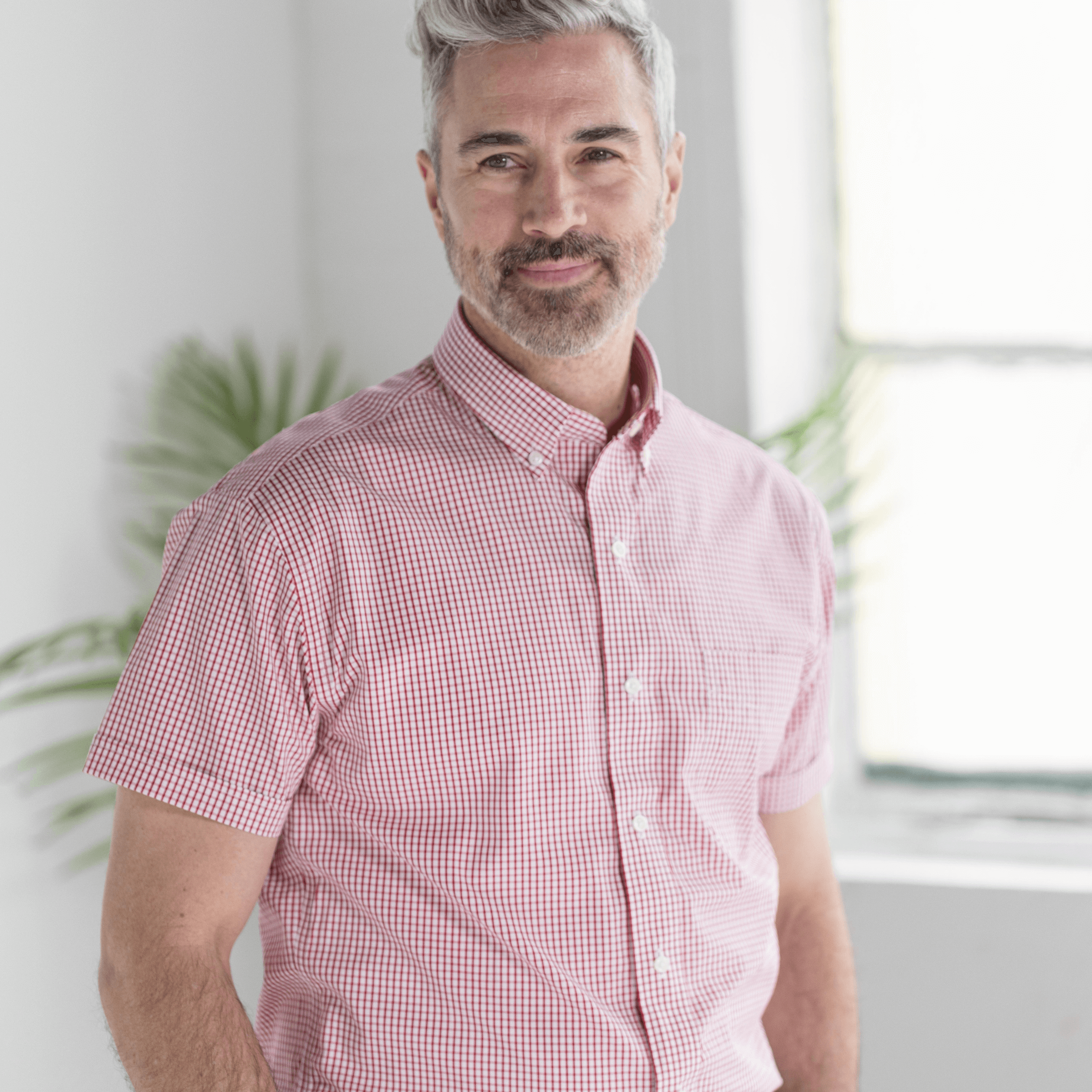 Man wearing a short sleeve red and white checked cotton shirt, featuring a button-down collar and a friendly smile.