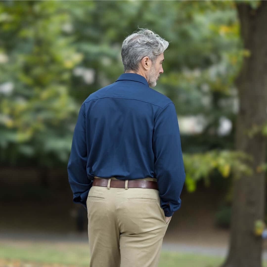 Man wearing adaptive true navy long sleeve cooling tech polo with pocket, seen from the back in a natural setting.