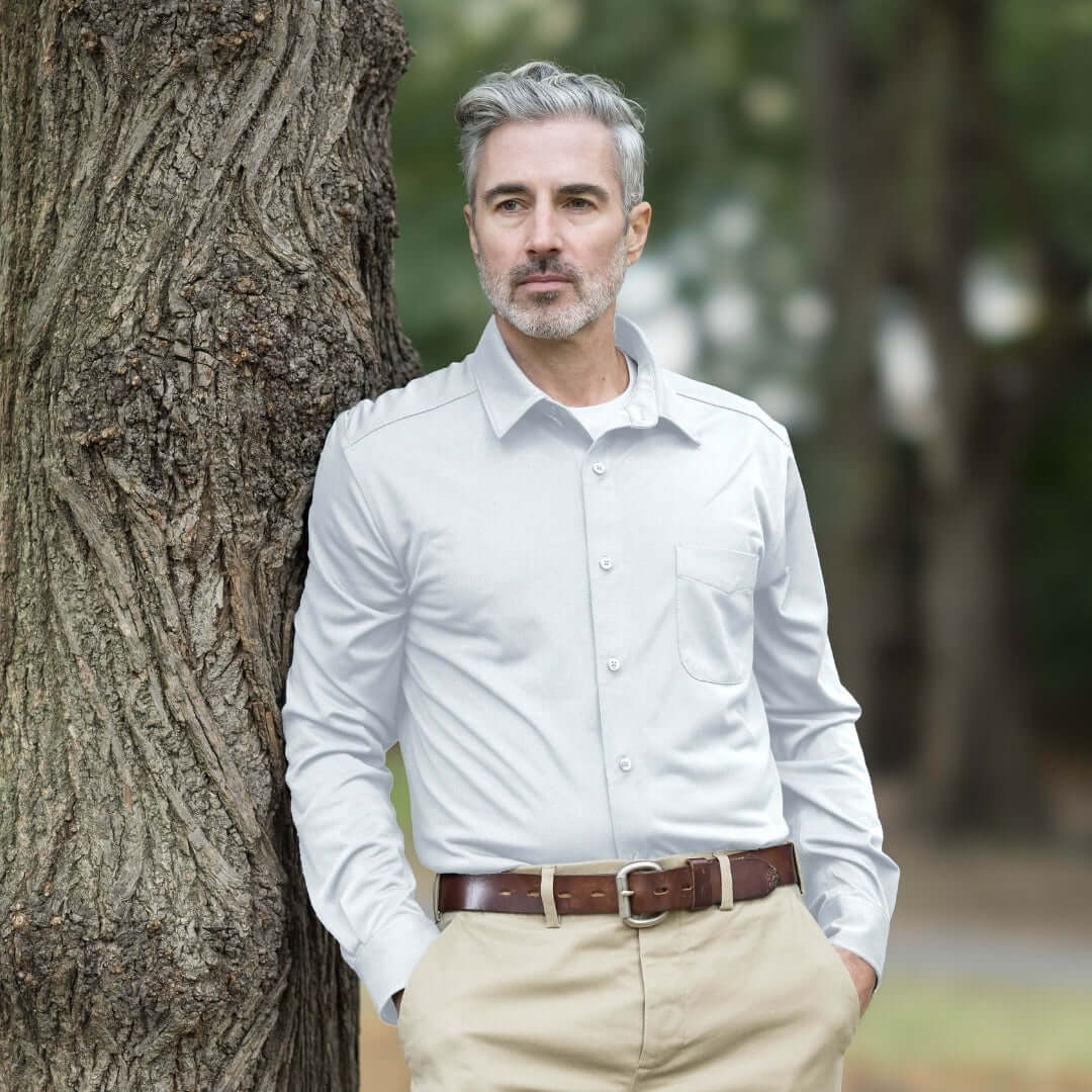 Adaptive White Magnetic Front Long Sleeve Cooling Adaptive Polo with Pocket worn by a man leaning against a tree.