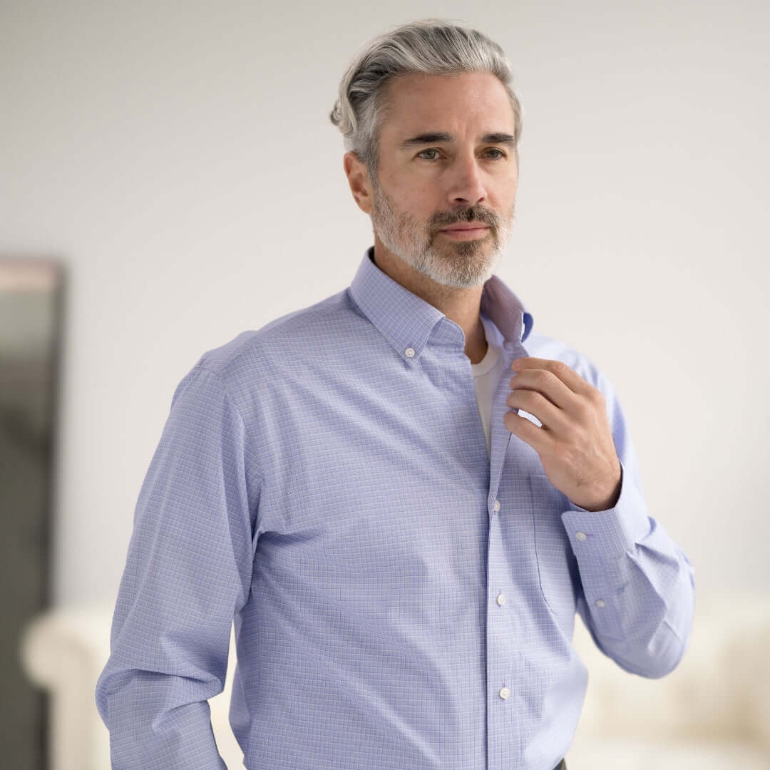 Stylish man adjusting his blue checkered dress shirt in a bright indoor setting.