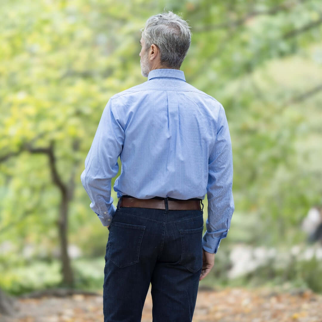 Back view of a man wearing a blue long sleeve button down shirt with magnetic closures in a park setting.