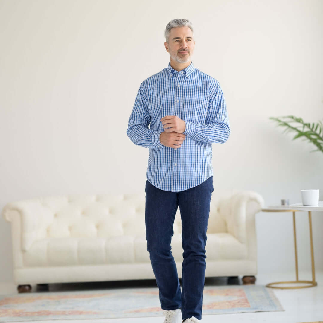 Man in a blue and white grid long sleeve button-down shirt with magnetic closures, standing in a bright living space.