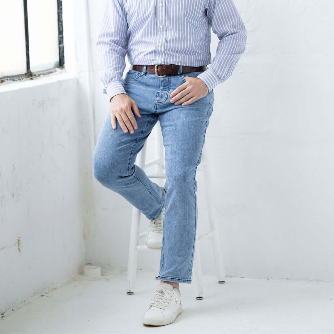 Man wearing light wash five pocket jeans with magnetic closures, sitting on a stool in a bright room.