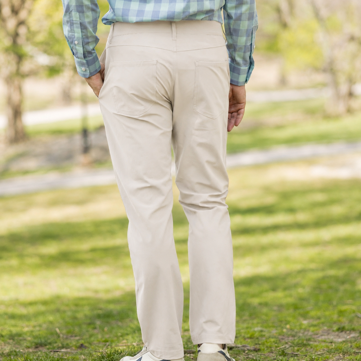 Back view of a man wearing Flat Front Adaptive Stretch Tech Pant with Magnetic Closures - Stone on a grassy area.