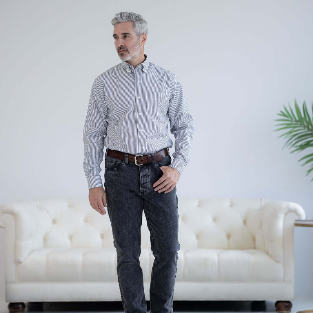 Man wearing a grey stripe long sleeve button down collar shirt with magnetic closures, standing in front of a sofa.