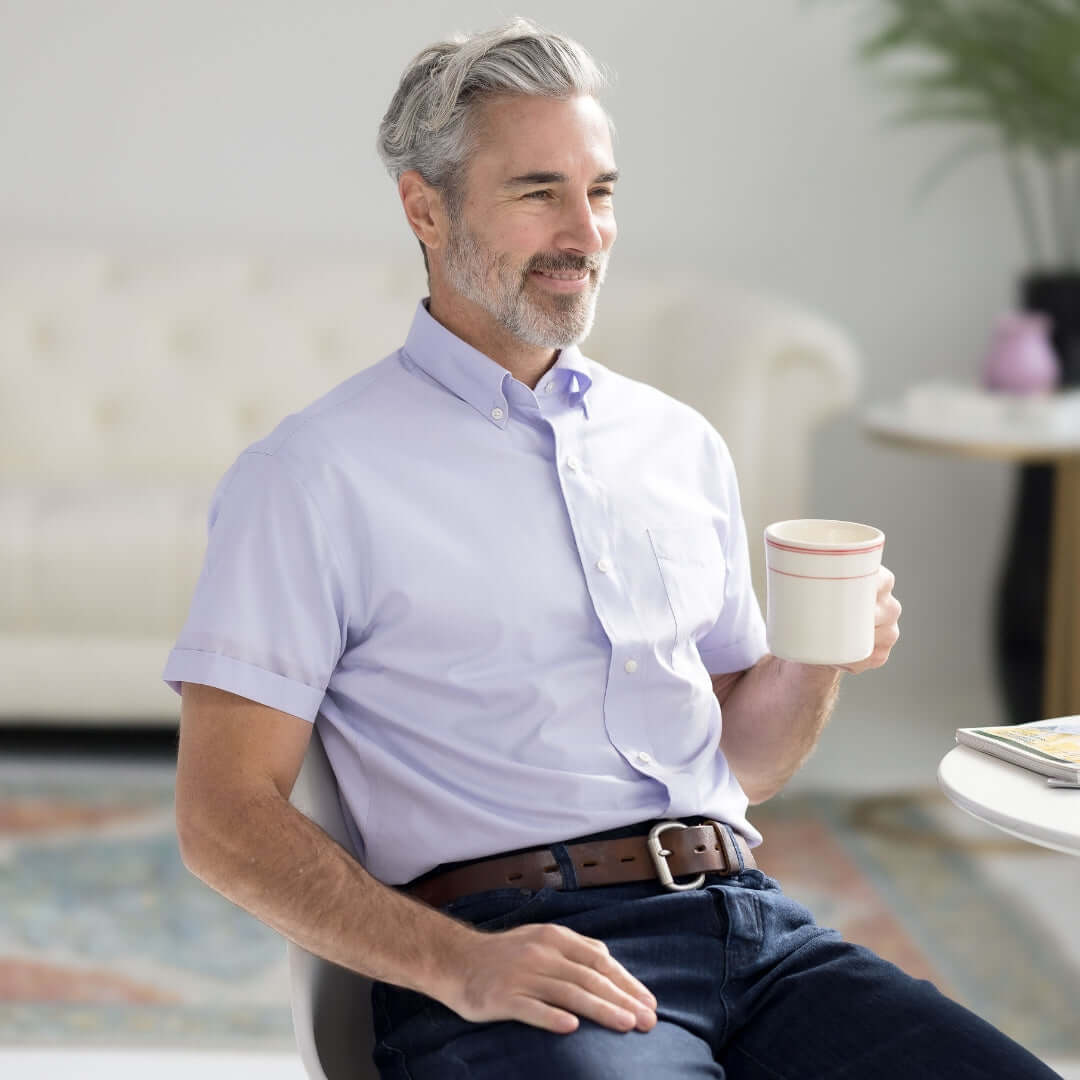 Man enjoying coffee in a lavender short sleeve button-down shirt, showcasing modern style and comfort.