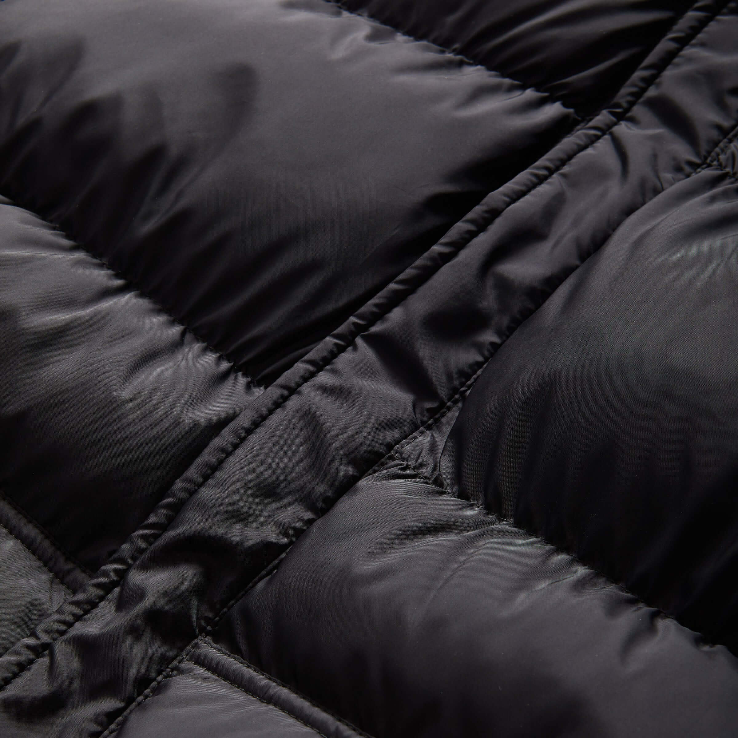 Close-up of black puffer coat fabric, highlighting water-resistant material and cozy quilted design.