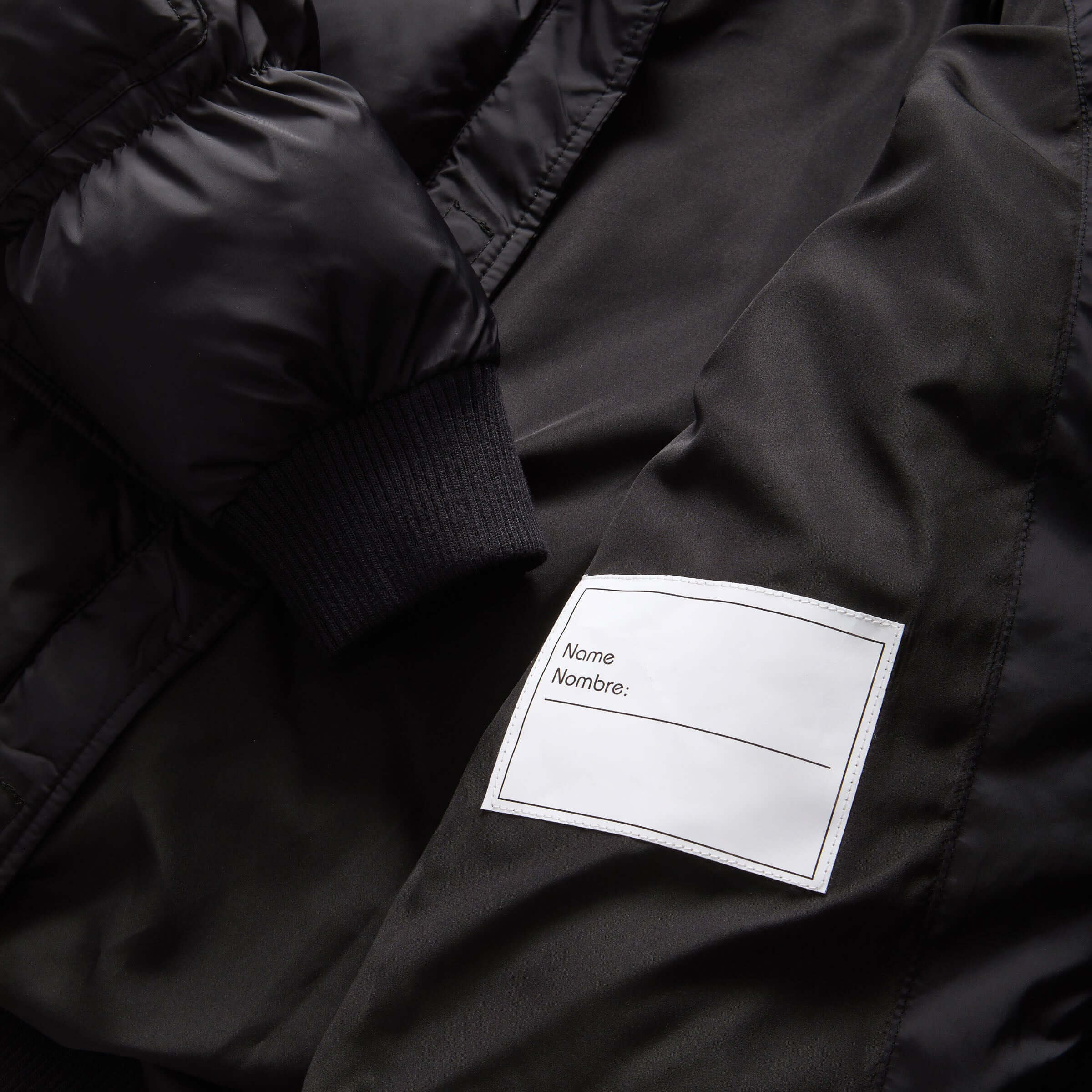 Interior label of a black kid's puffer coat, featuring a name tag for personalization.