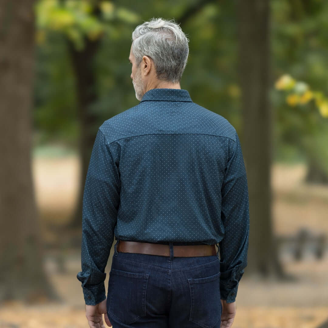 Man wearing a blue check long sleeve shirt, viewed from the back, in a natural outdoor setting with trees.