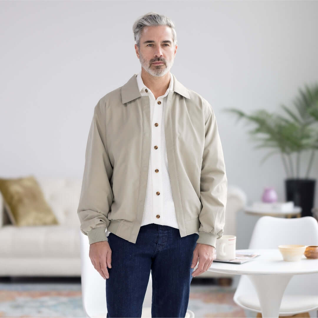 Man wearing a light stone colored MagnaReady x Weatherproof Golf Jacket in a cozy indoor setting.