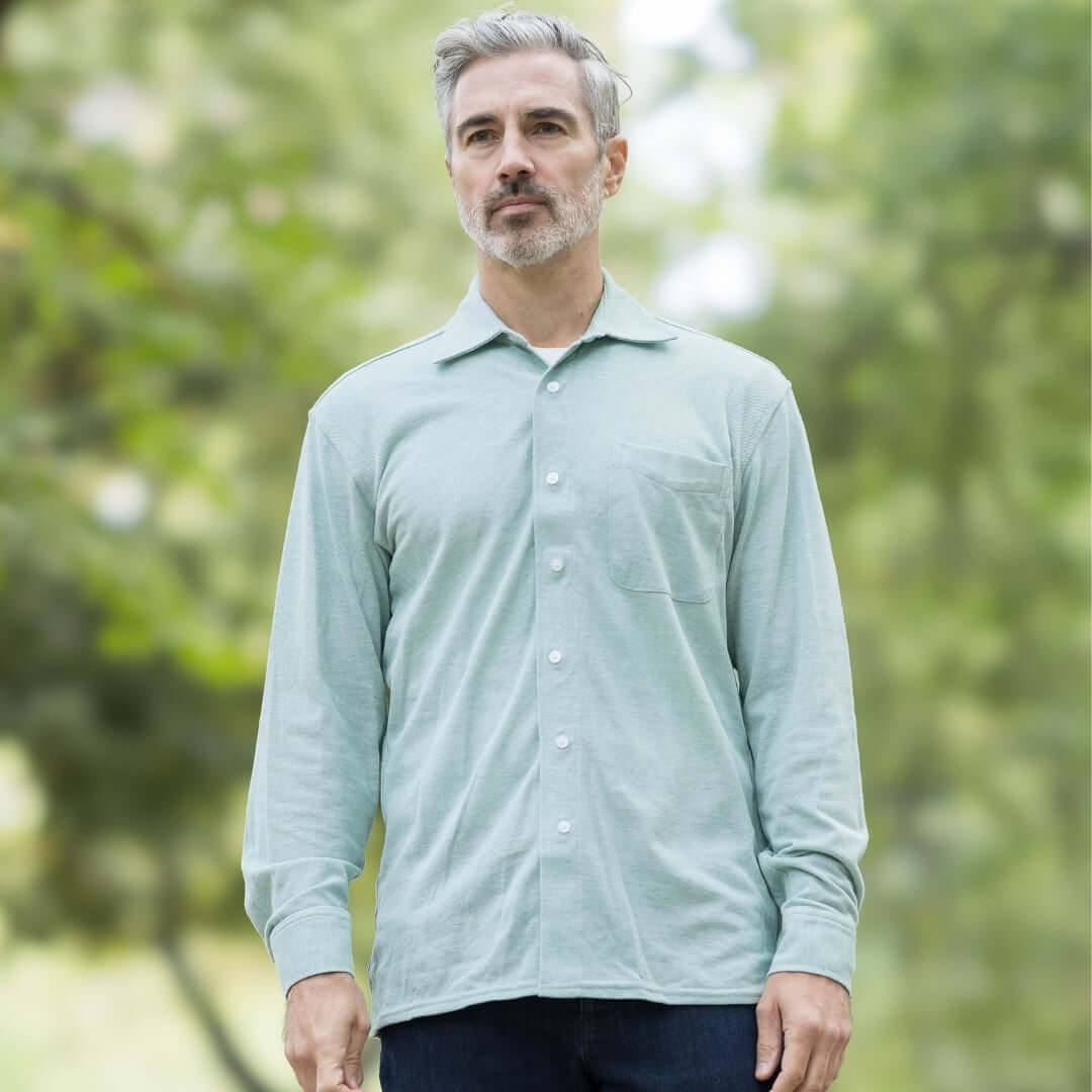 Man wearing Ivy Green Magnetic Front Knit Oxford Shirt with long sleeves and pocket, set against a blurred natural background.