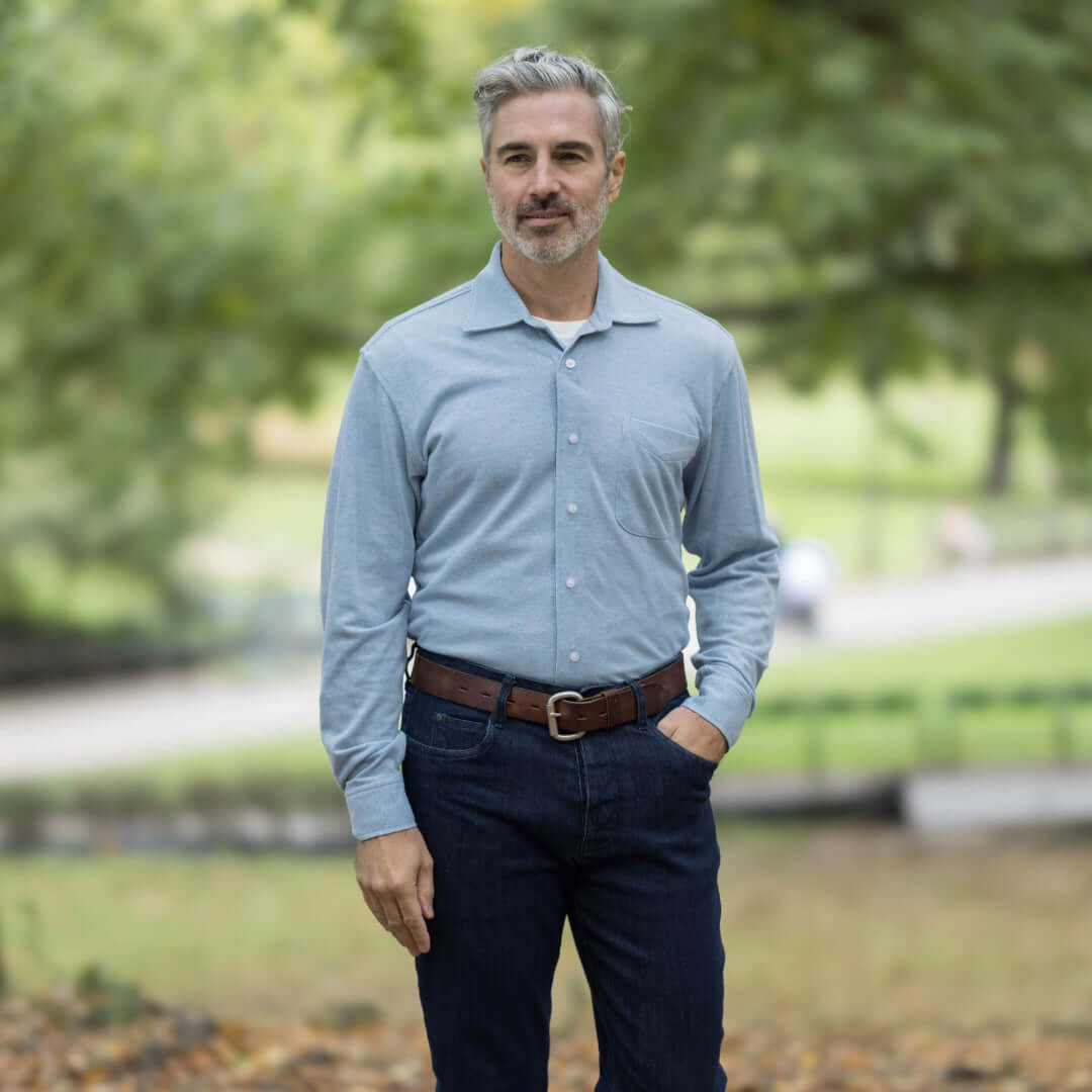 Man in sky blue long sleeve Oxford shirt with magnetic closure, styled casually outdoors.