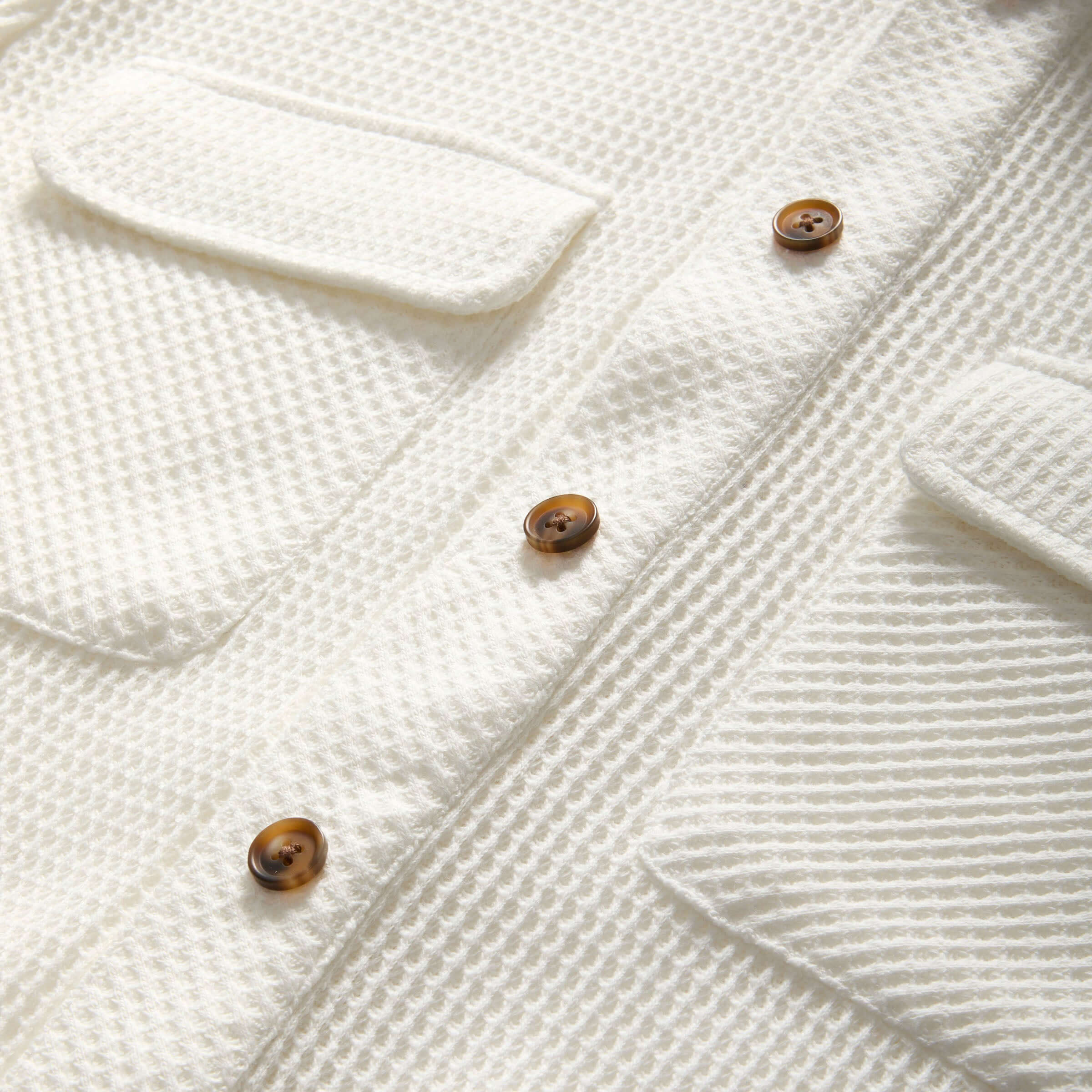 Close-up of a white waffle weave casual shirt featuring dual oversized pockets and brown buttons.