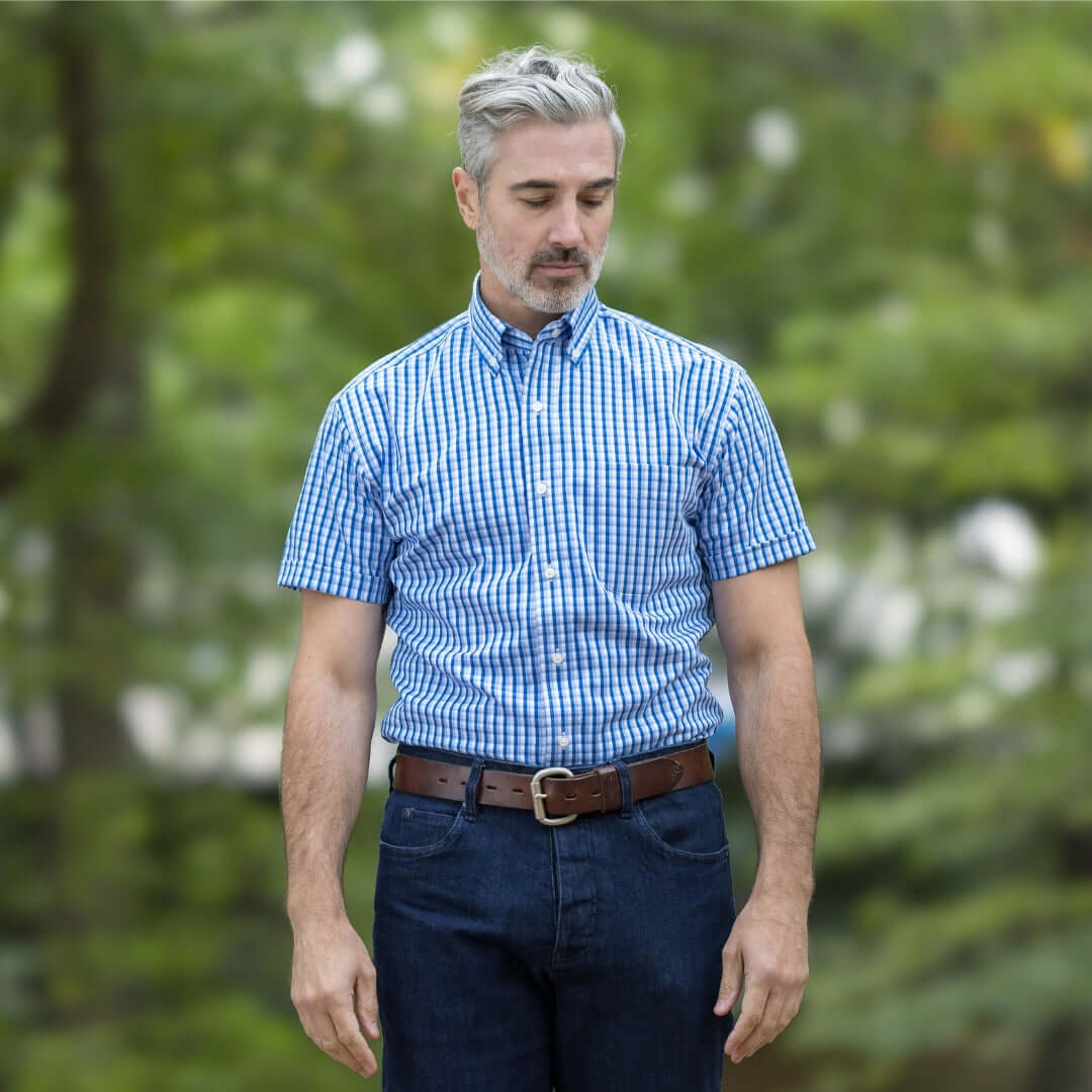 Man wearing a short sleeve blue and white check cotton shirt outdoors, looking relaxed in a natural setting.