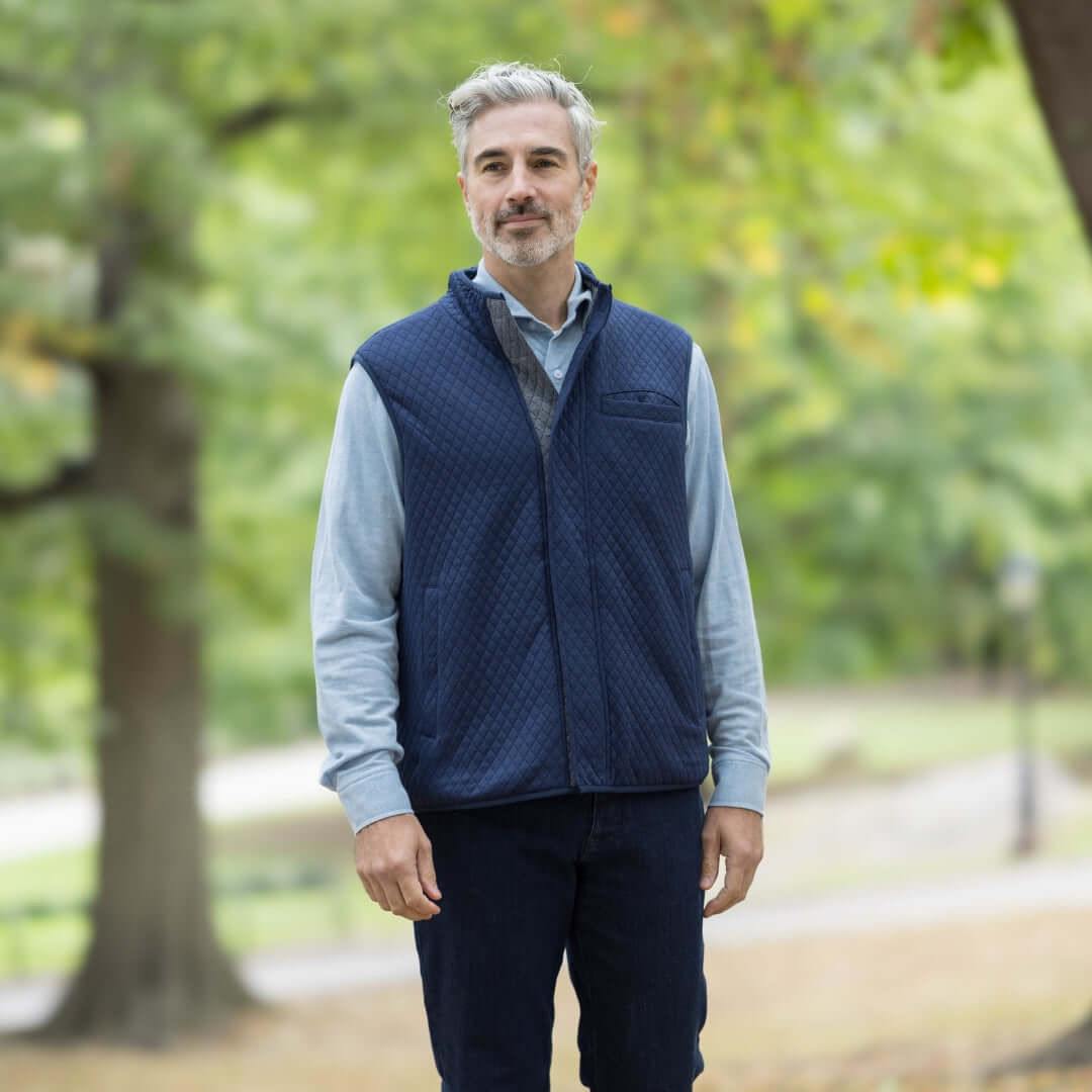 Man wearing a navy quilted vest over a light blue shirt in a natural setting.