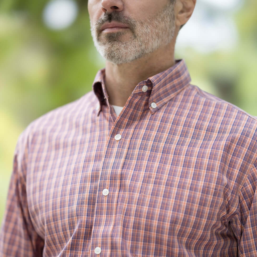 Close-up of a man wearing an orange long sleeve button-down collar shirt with a plaid pattern and magnetic closures.