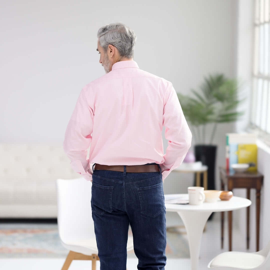 Back view of a man wearing a pink long sleeve button down collar shirt in a modern living space.
