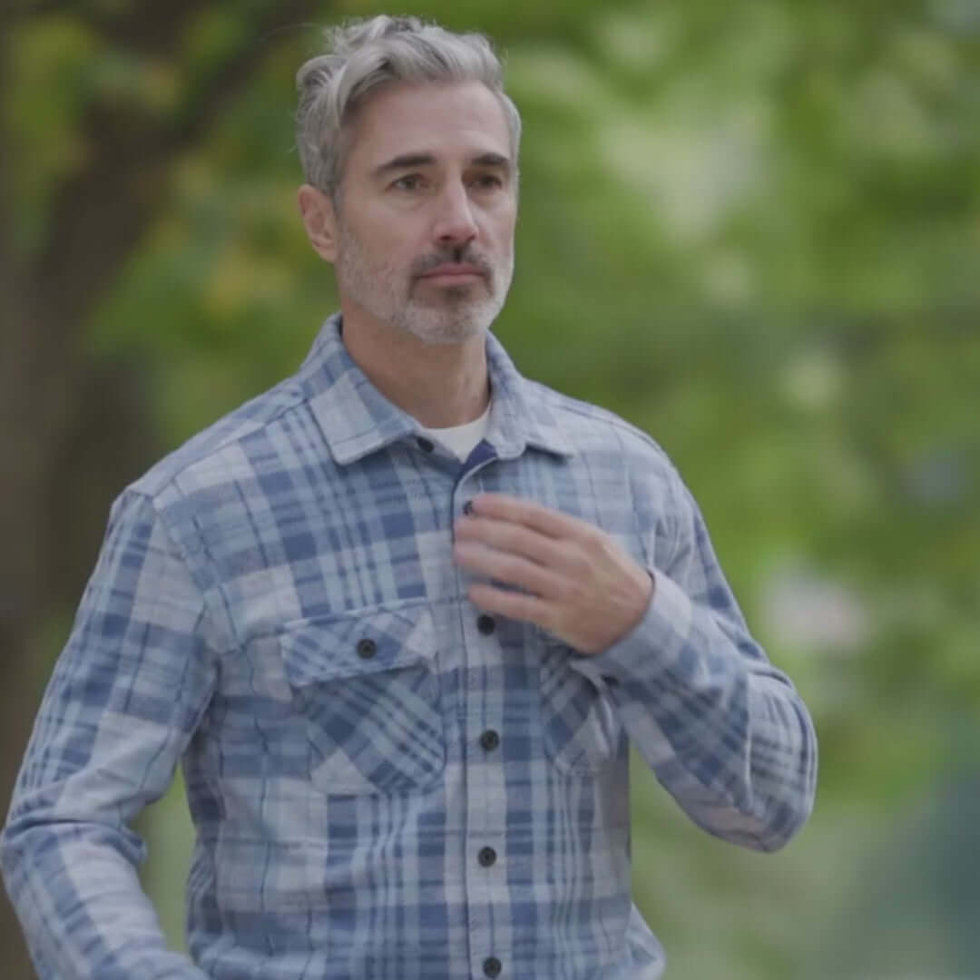 Man walking outdoors in an adaptive pale blue plaid flannel shirt layered for style and comfort.
