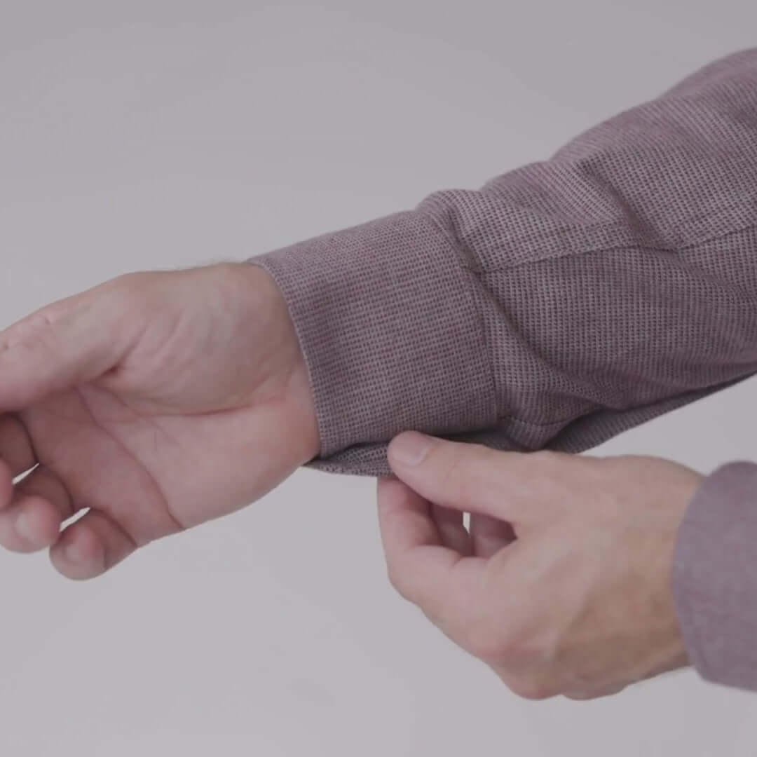 Close-up of a hand adjusting the cuff of a red and grey long sleeve shirt with magnetic closures.