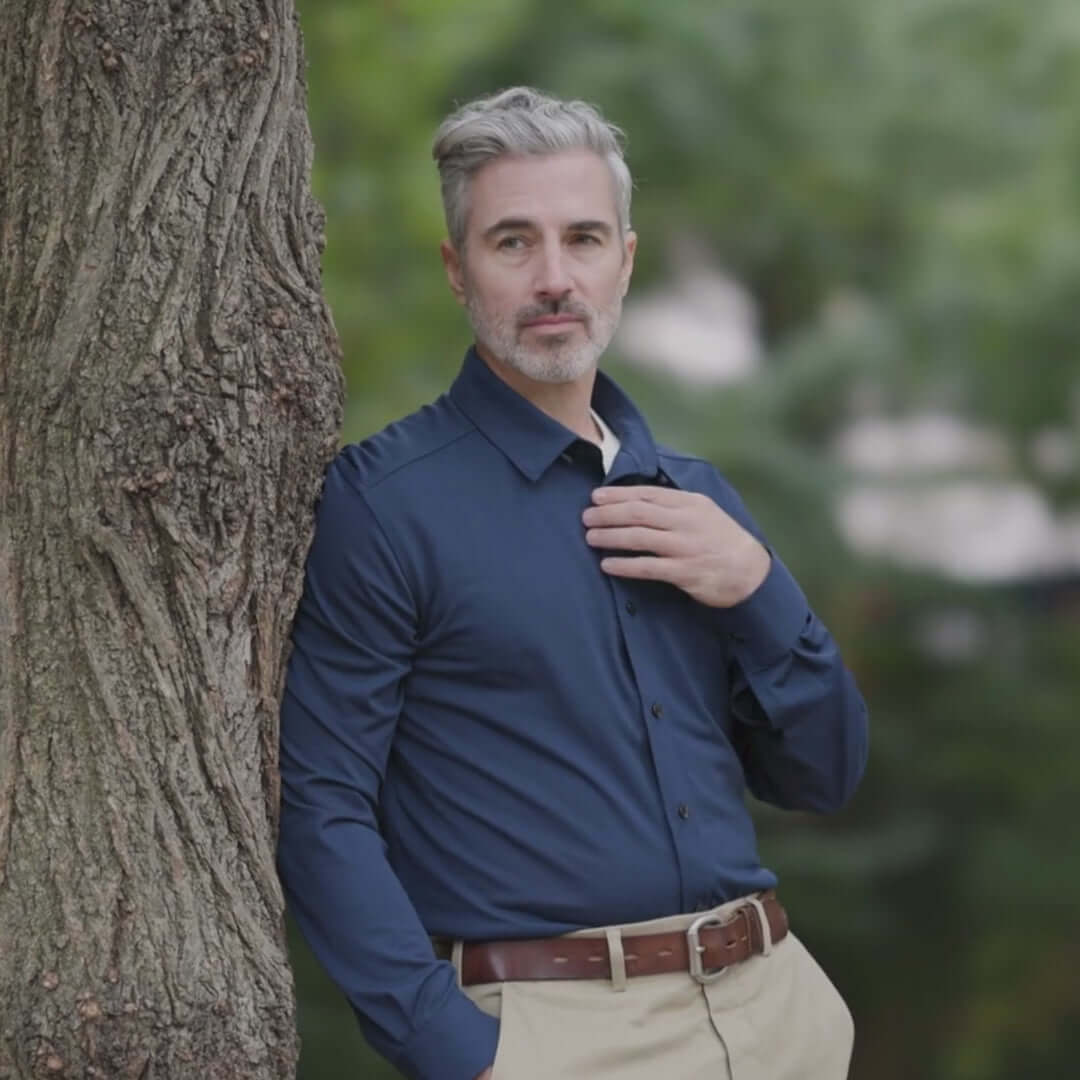 Man in navy long sleeve shirt standing by a tree, showcasing a casual yet stylish look.