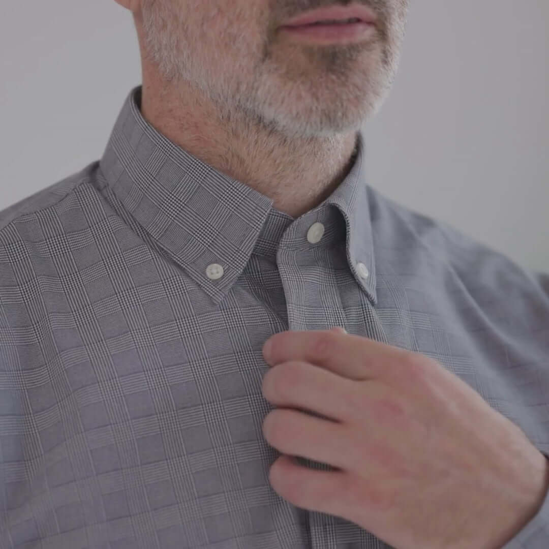 Model adjusting collar of a navy plaid button-down shirt with adaptive magnetic closures, perfect for limited mobility.