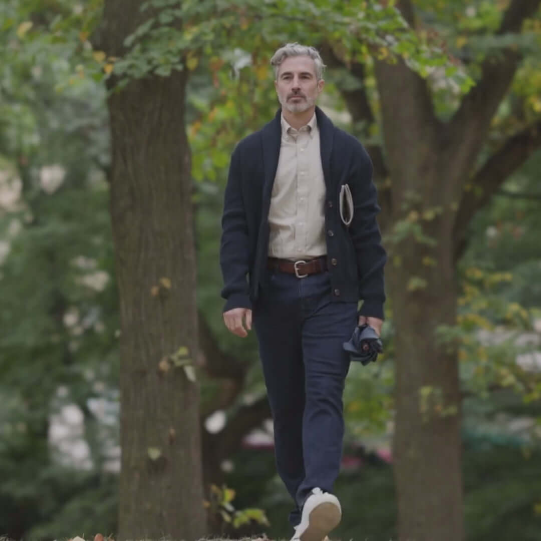 Man walking in a park wearing a navy cardigan, button-up shirt, and casual pants, showcasing comfort and style.