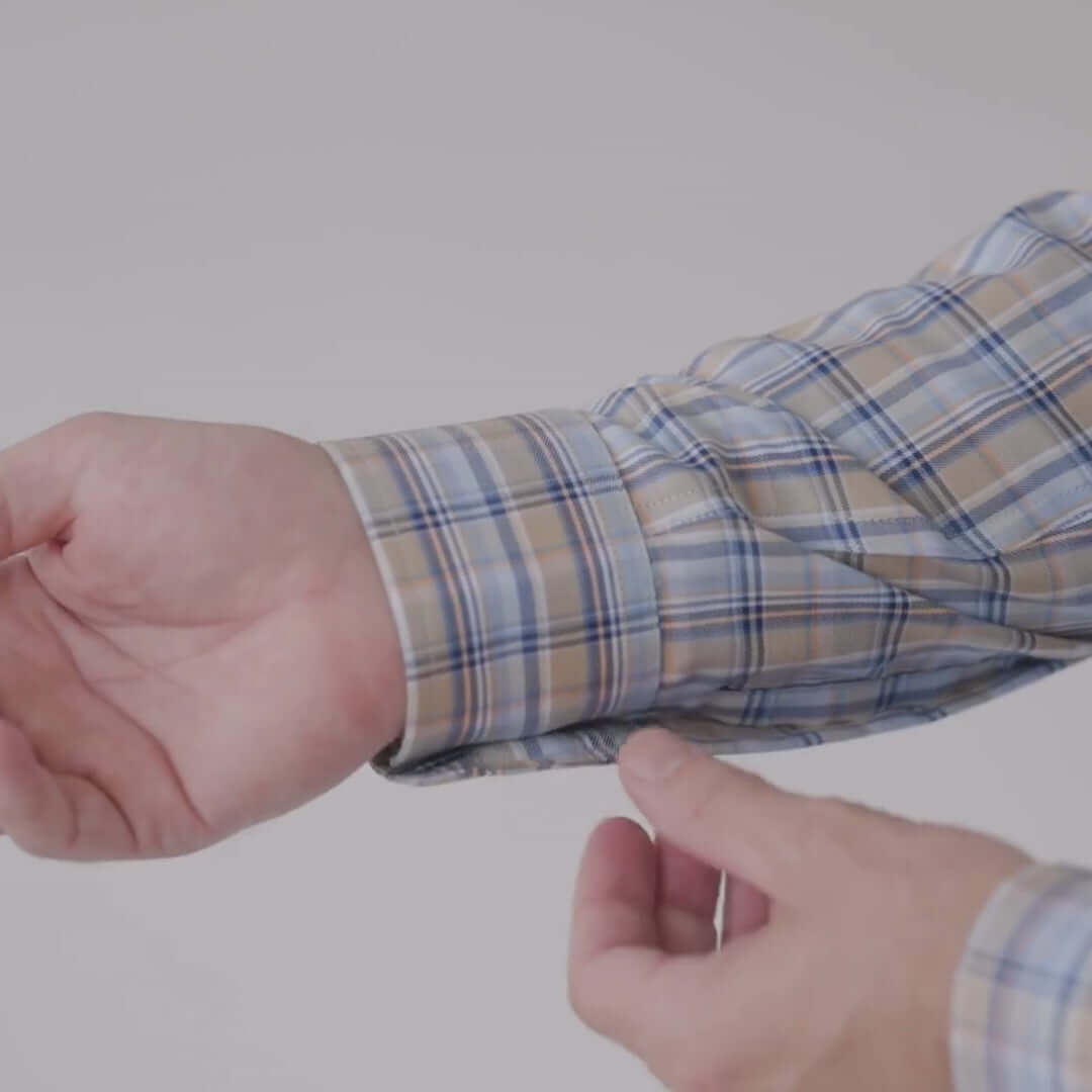 Close-up of a hand adjusting the sleeve of a blue and brown plaid long sleeve button-down shirt.