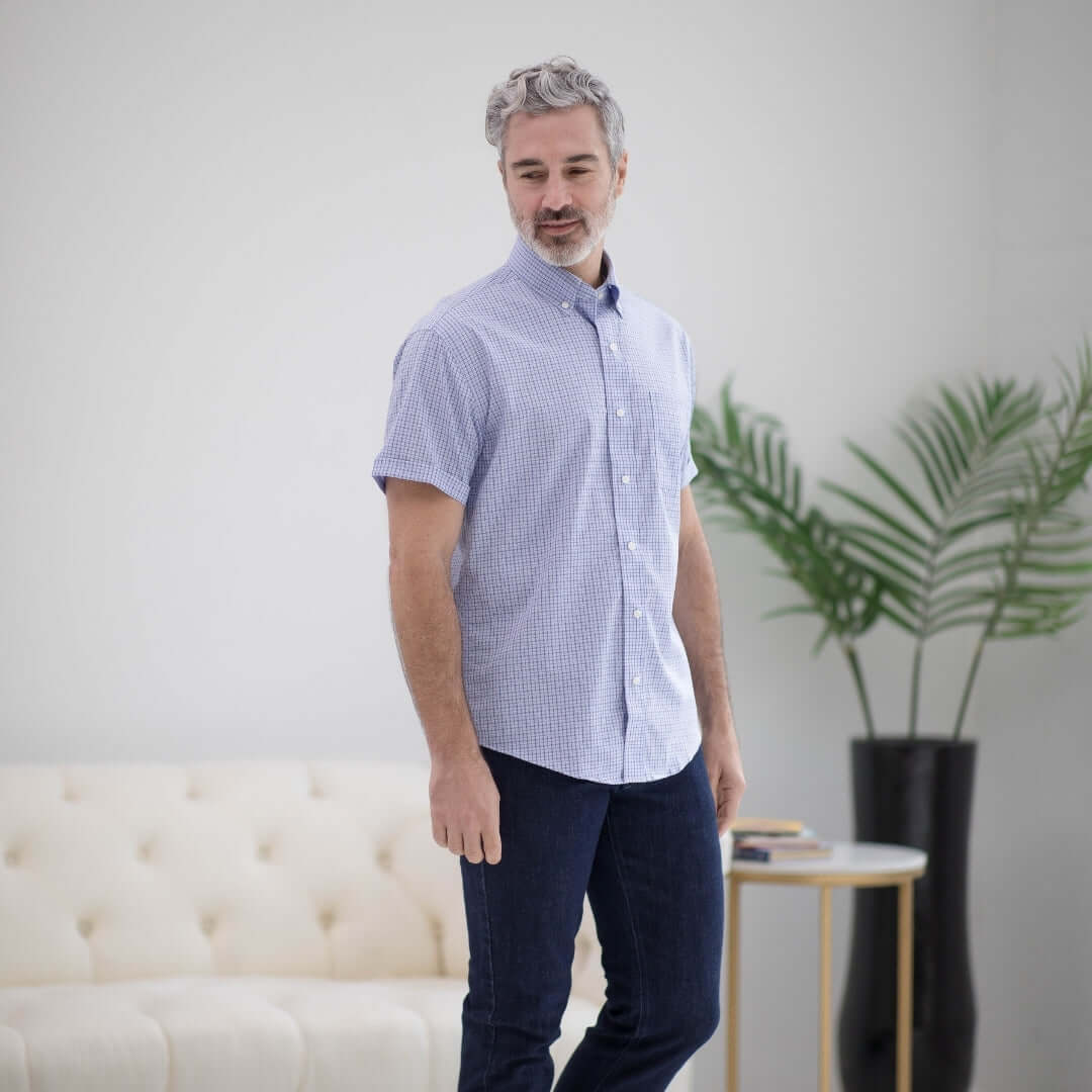 Man wearing a short sleeve blue and red check cotton shirt with magnetic closures, posing in a modern living space.