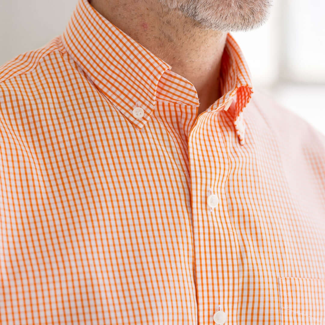 Close-up of men's orange and white gingham cotton shirt with button-down collar, showcasing adaptive design.