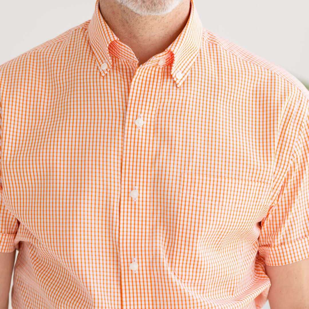 Close-up of a man wearing a short sleeve orange and white gingham cotton shirt with a button-down collar.
