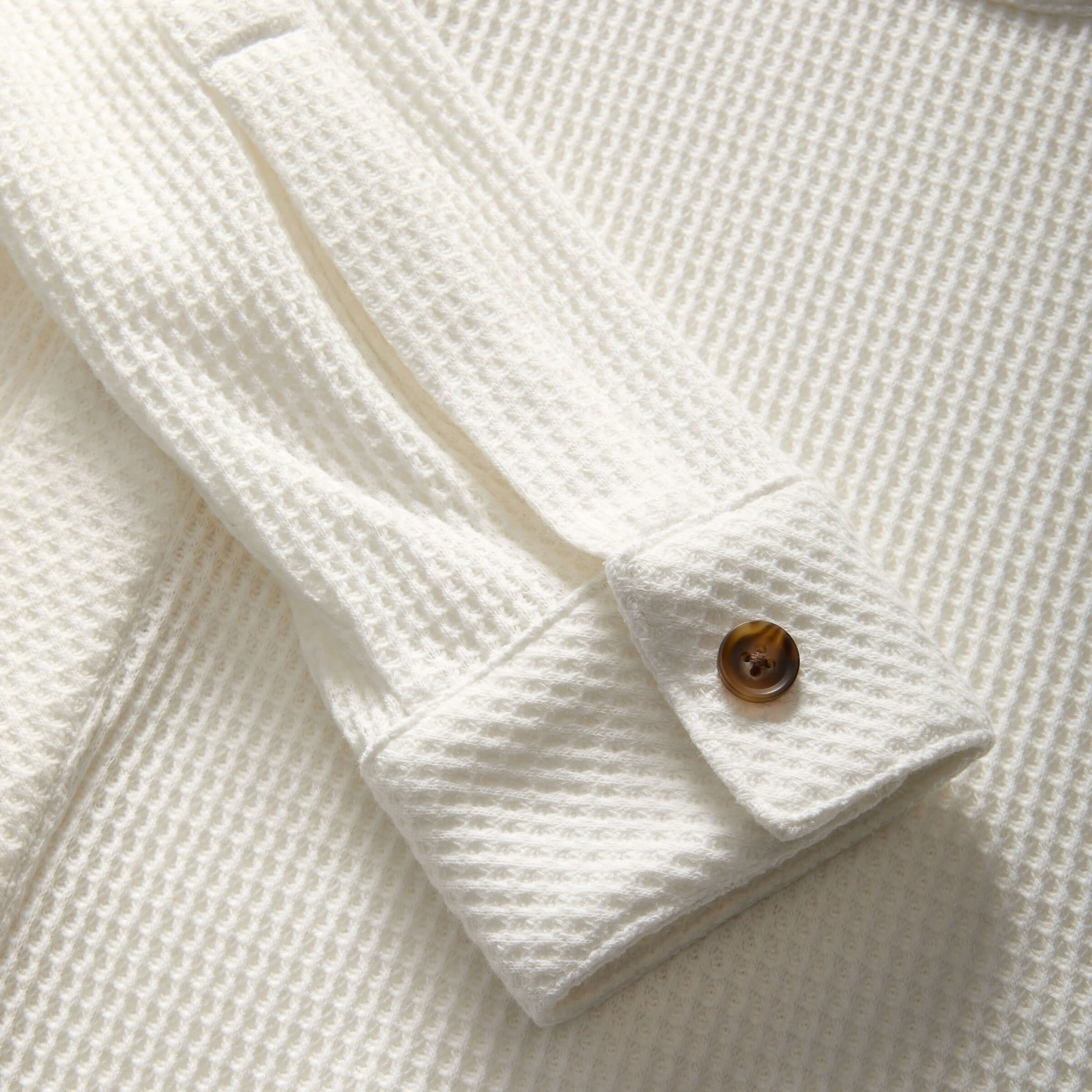 Close-up of white waffle weave fabric shirt sleeve with button detail, showcasing soft texture and casual style.