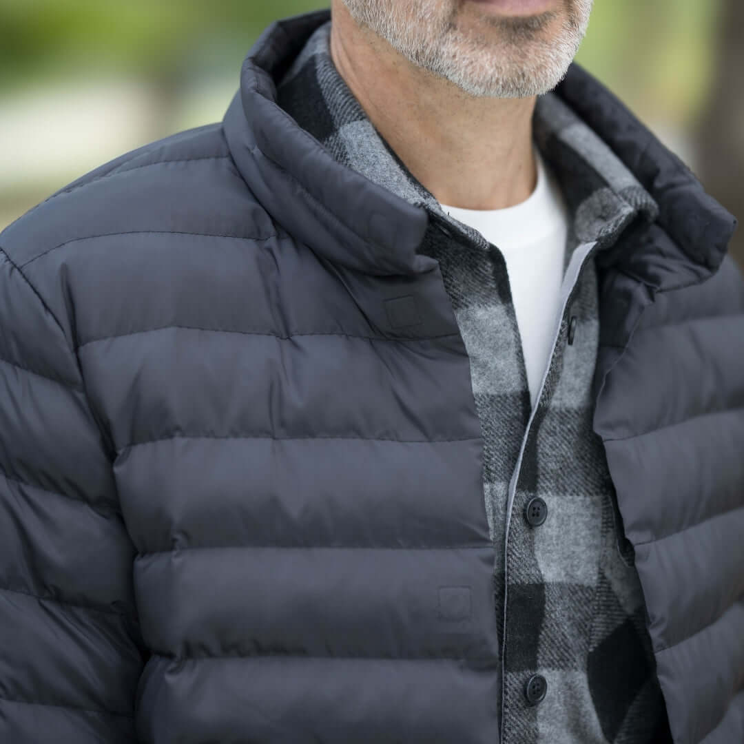 Close-up of a man wearing a black weatherproof puffer jacket over a flannel shirt.