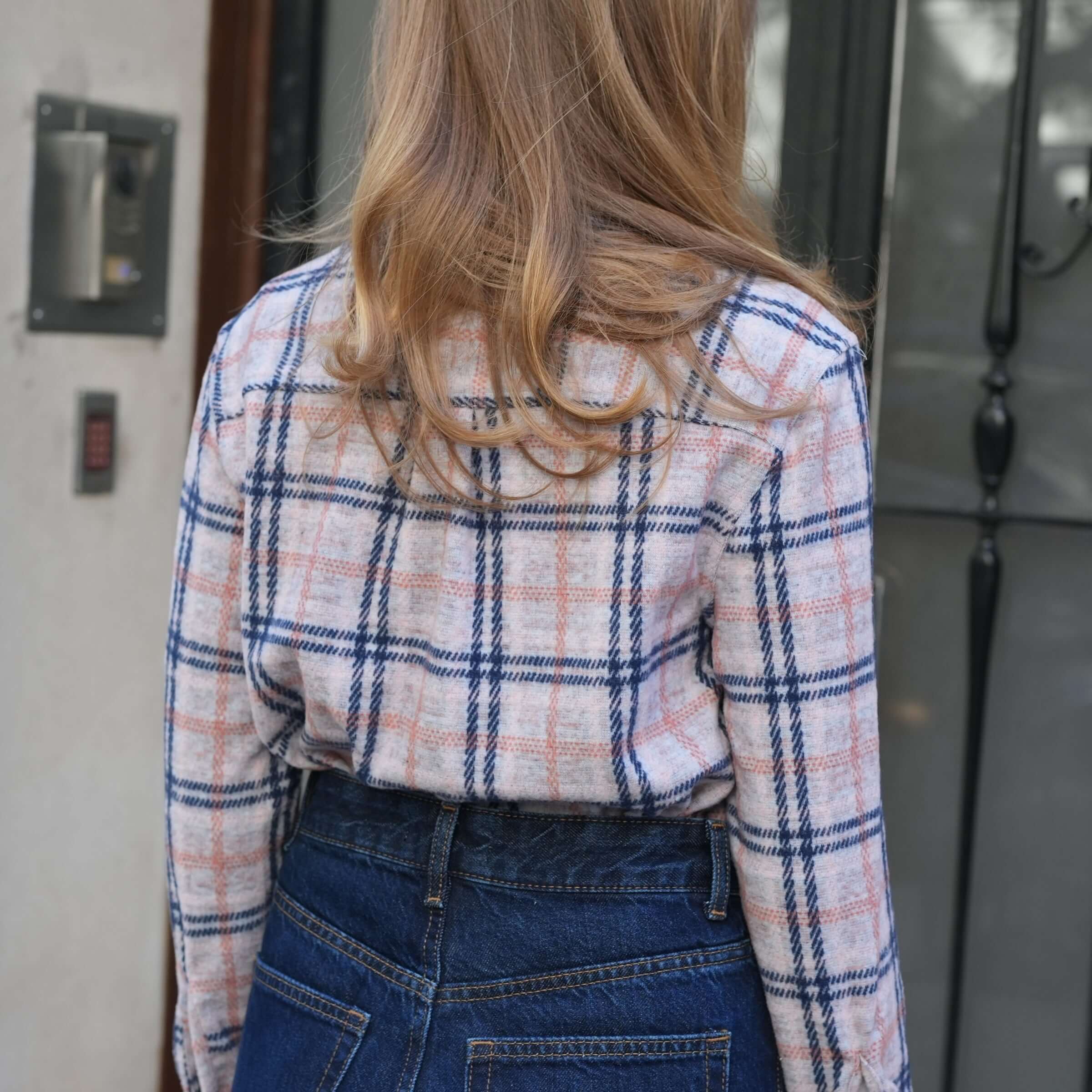 Back view of a woman wearing a pink, navy, and gray plaid flannel shirt paired with denim.