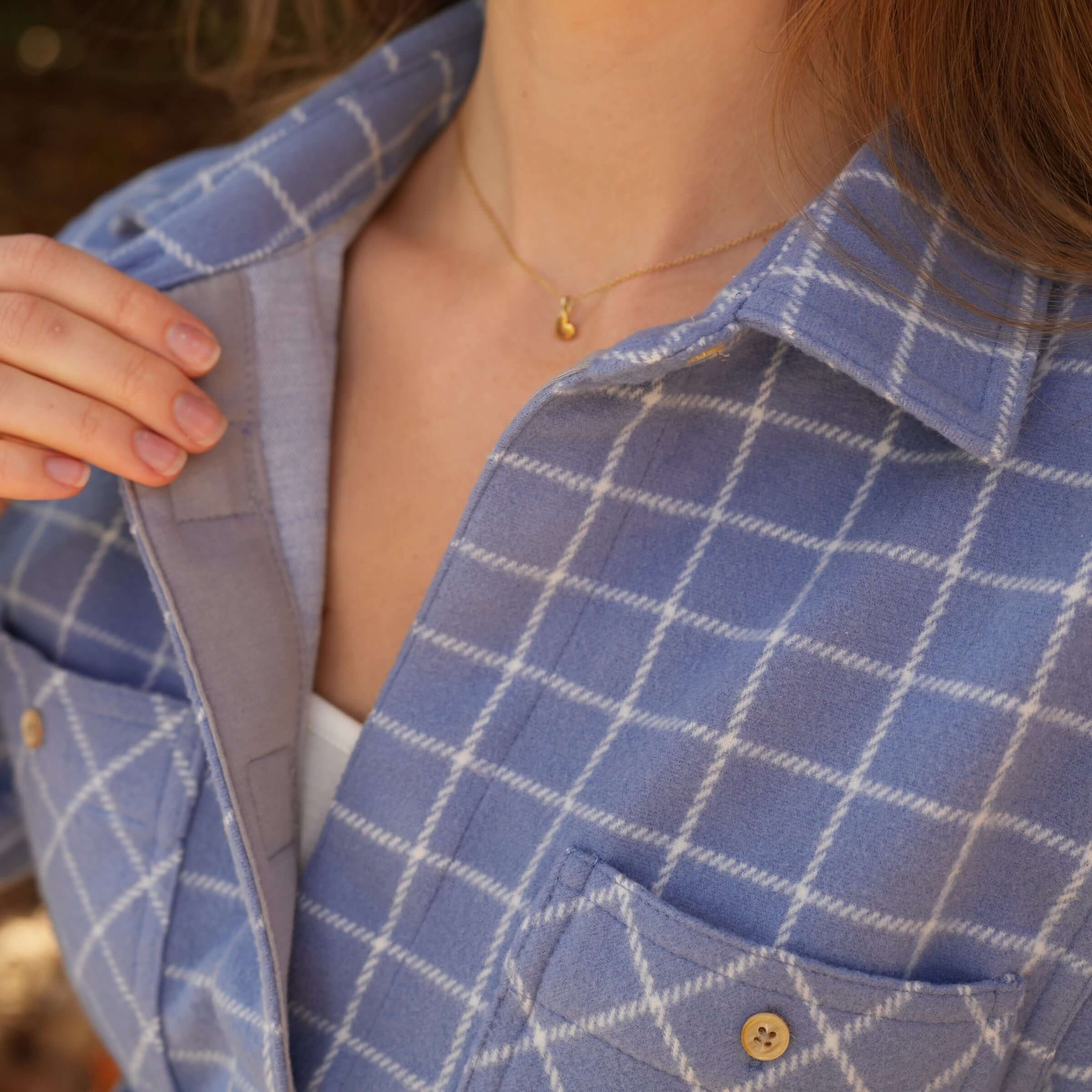 Close-up of a woman's blue and white flannel shirt, highlighting its stylish curved hem and comfortable fit.