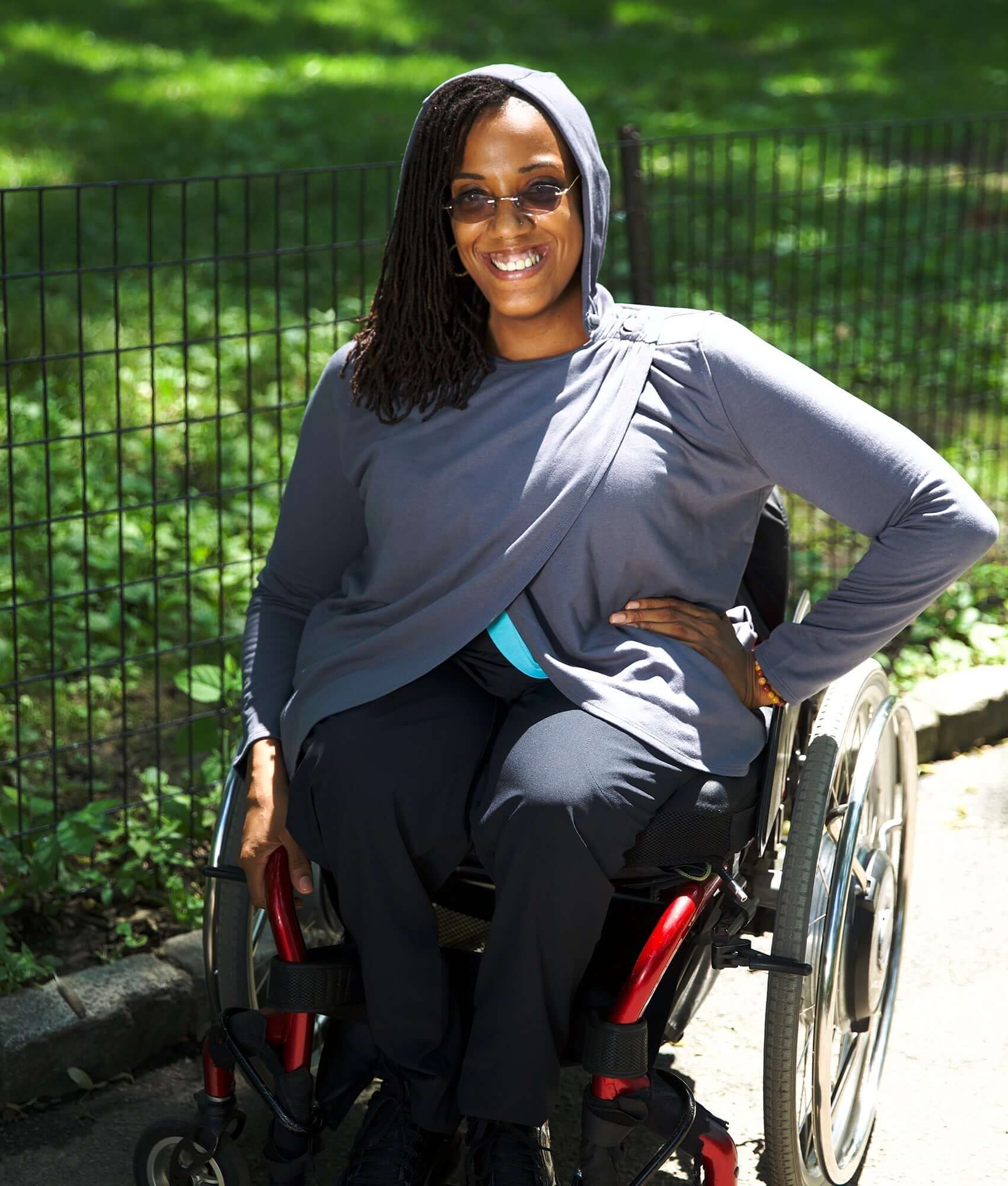 Woman in a wheelchair wearing the Women's Adaptive Hooded Wrap Cardigan in a park, showcasing comfort and style.
